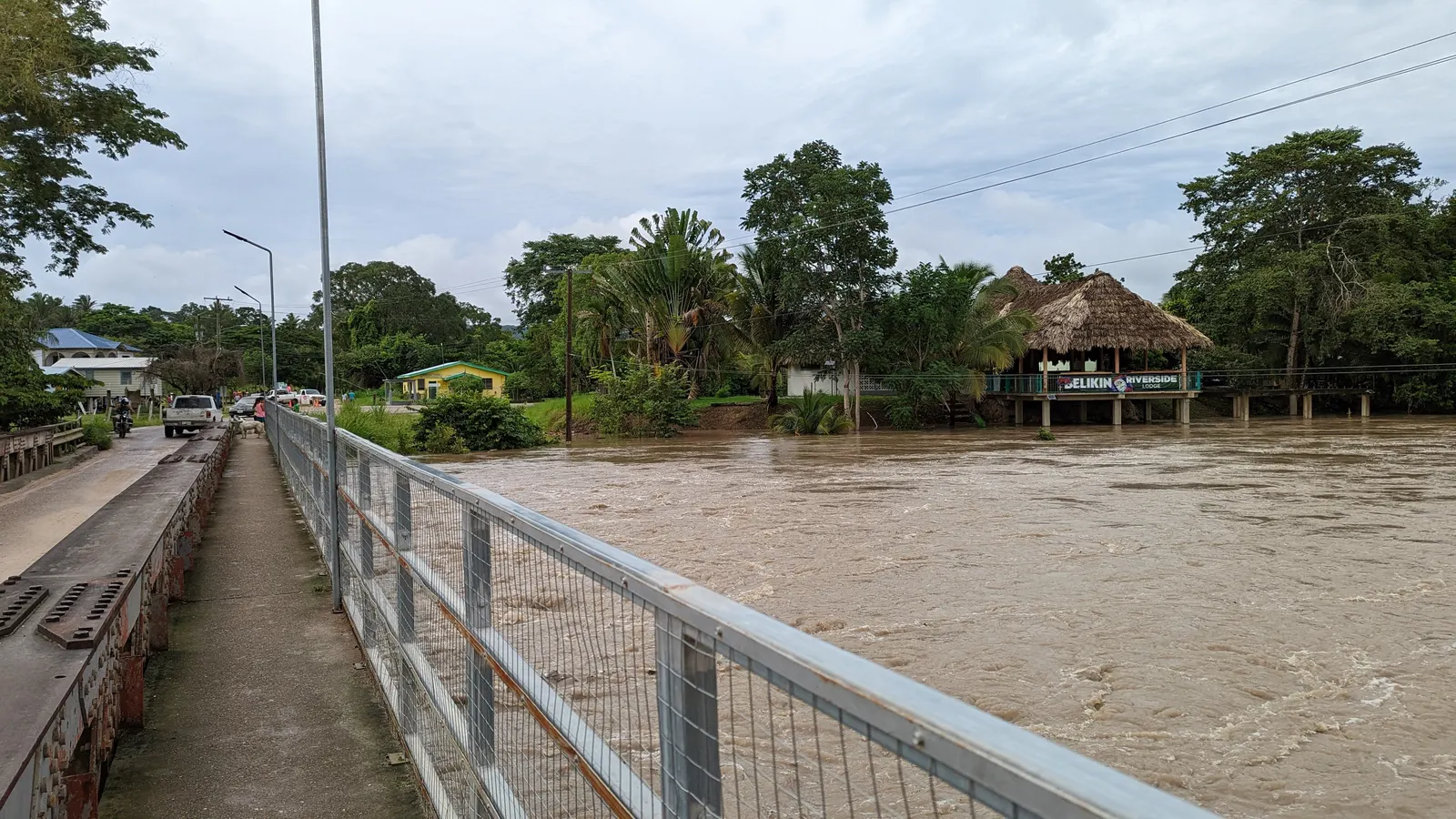 The swollen Mopan River running under the Bullet Tree Falls bridge in Cayo, Belize, with a riverside lodge on the far bank