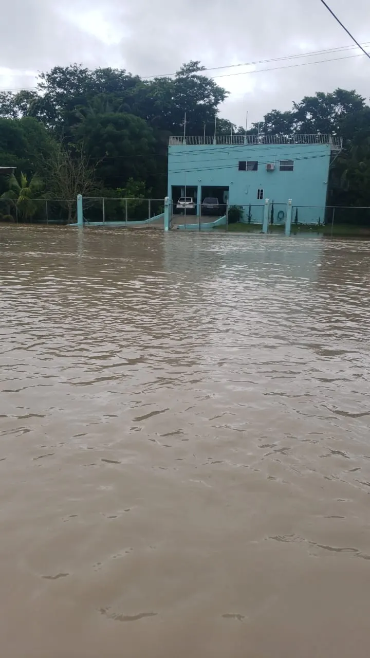 Floodwater filling the yard of a house in Belize, reaching the gate and the base of the building