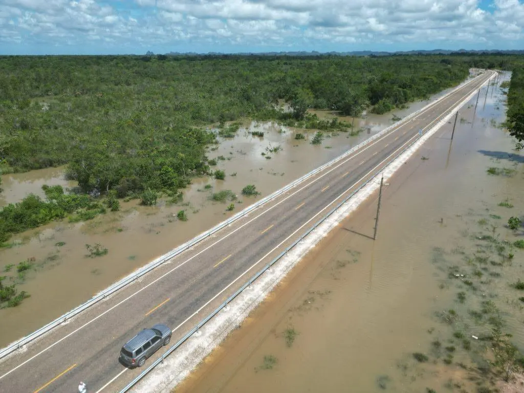 Aerial view of a Belize highway running as a raised causeway through floodwater covering the surrounding bush on both sides