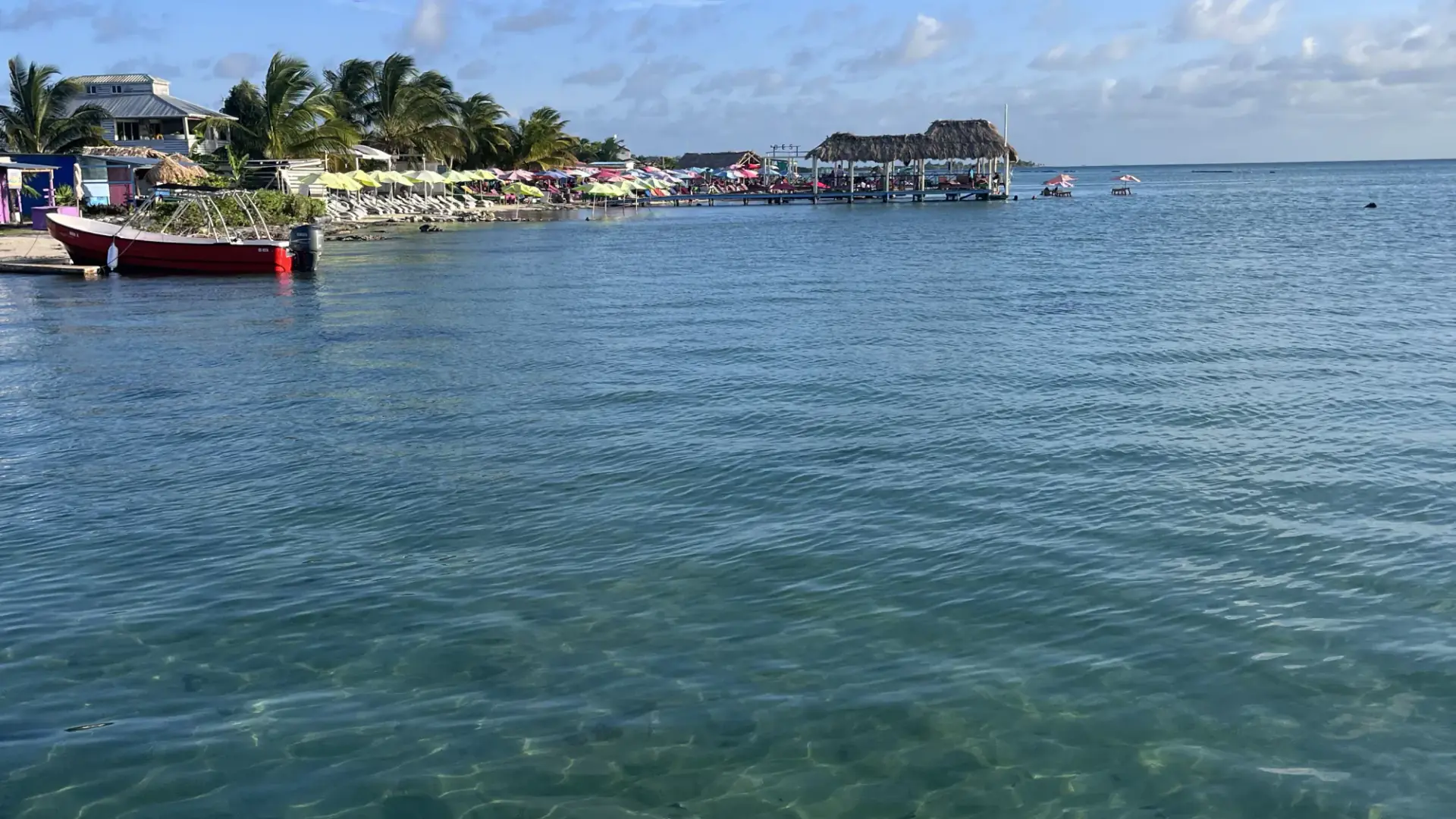 A wooden dock over clear shallow water off San Pedro, with boats moored beyond