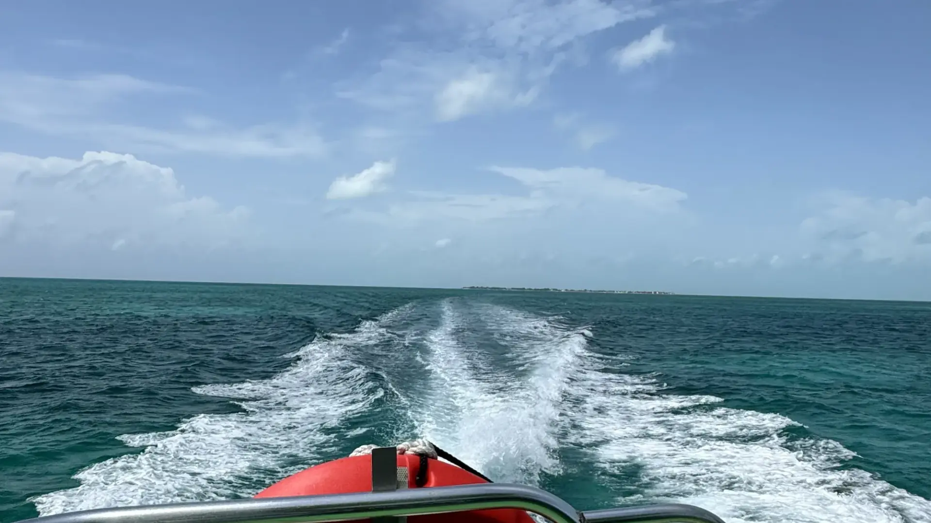 The wake of a Belize water taxi crossing open sea toward a low caye on the horizon