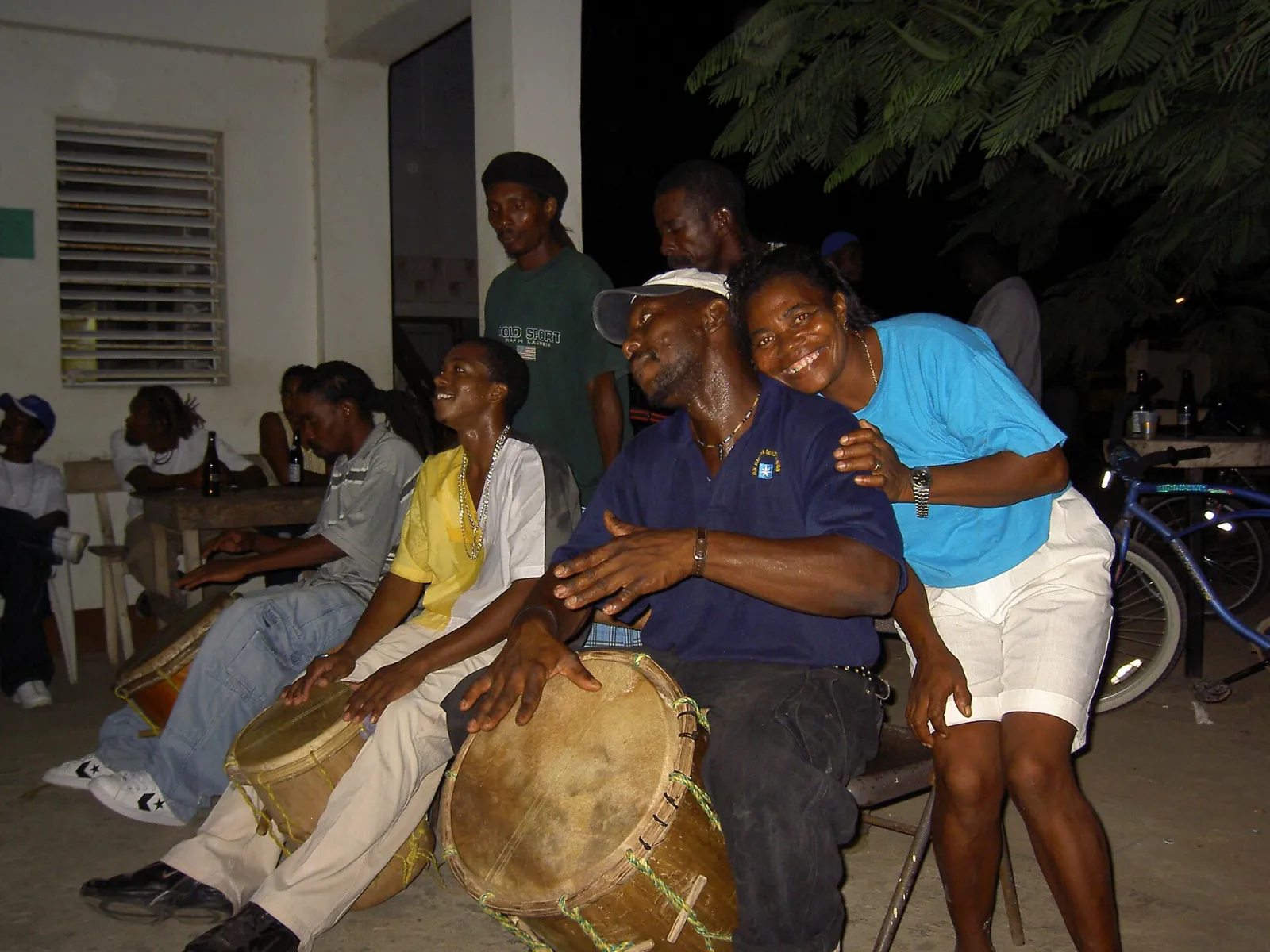 Garifuna drummers playing hand drums at a night session in Belize while a smiling woman hugs one drummer