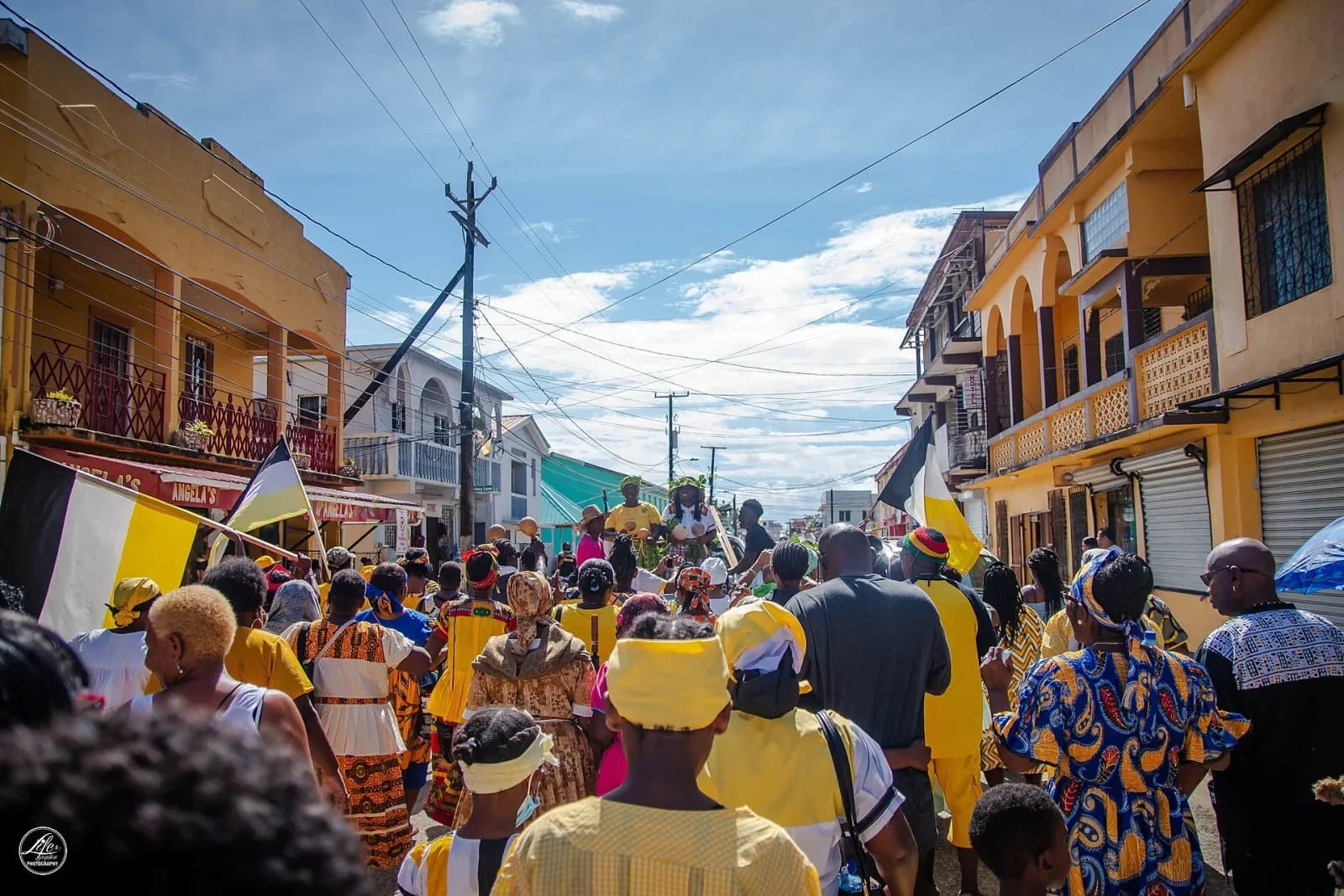 Crowd in yellow, white and black carrying Garifuna flags in a Settlement Day procession in Dangriga, Belize