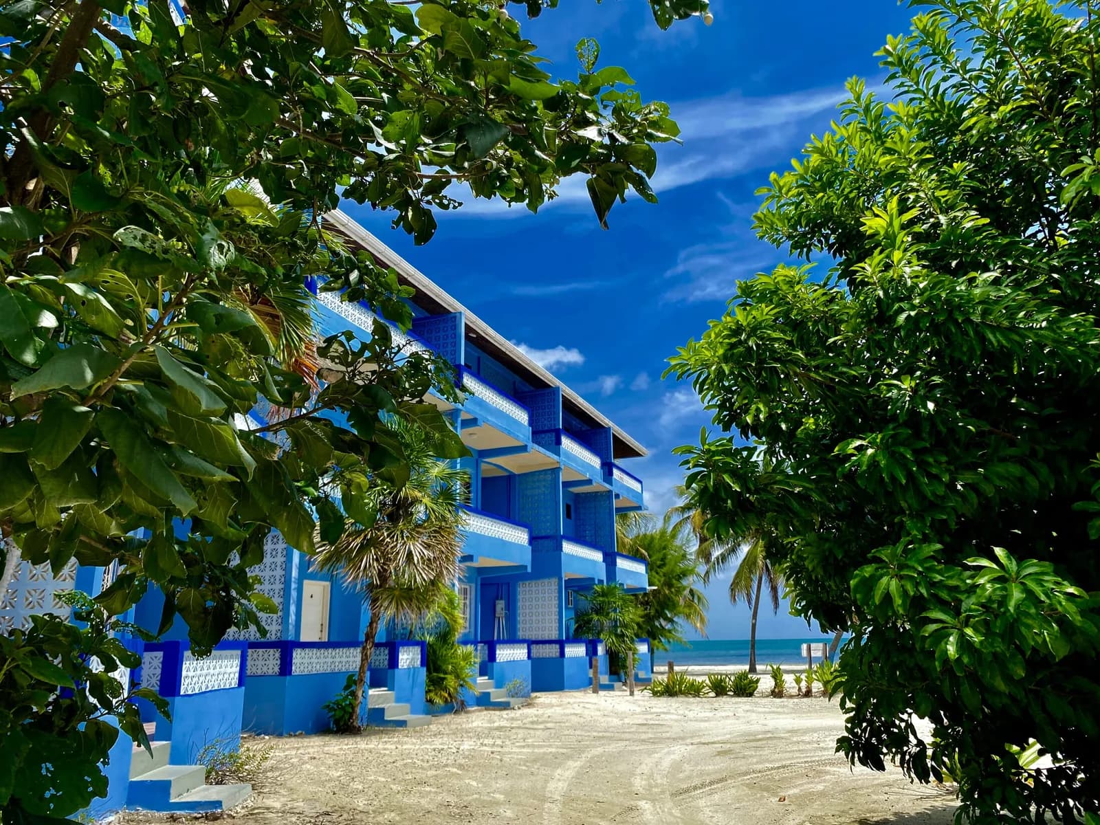 Anchorage Beach Resort's blue guest building framed by tropical trees with the Caribbean Sea visible behind it