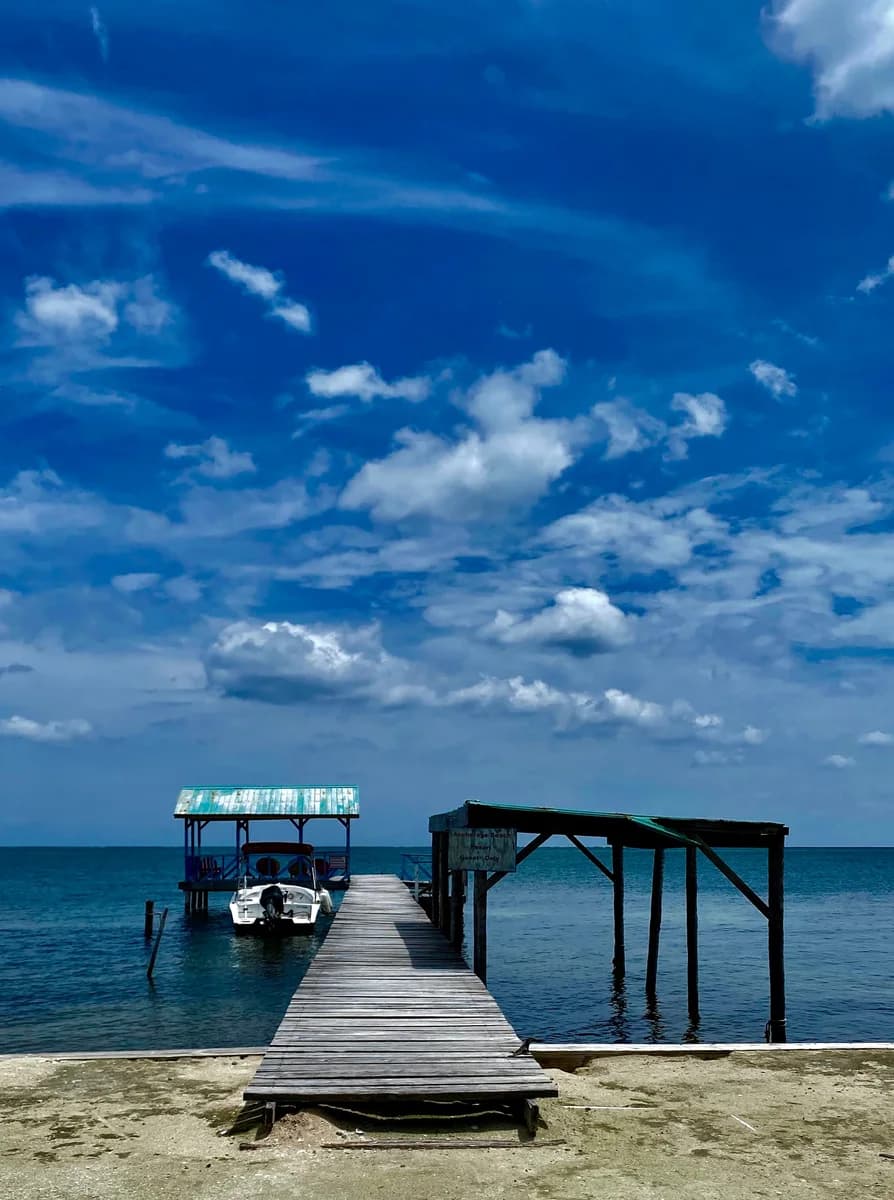 Anchorage Beach Resort's private dock with a boat moored under a wide blue sky, Caye Caulker