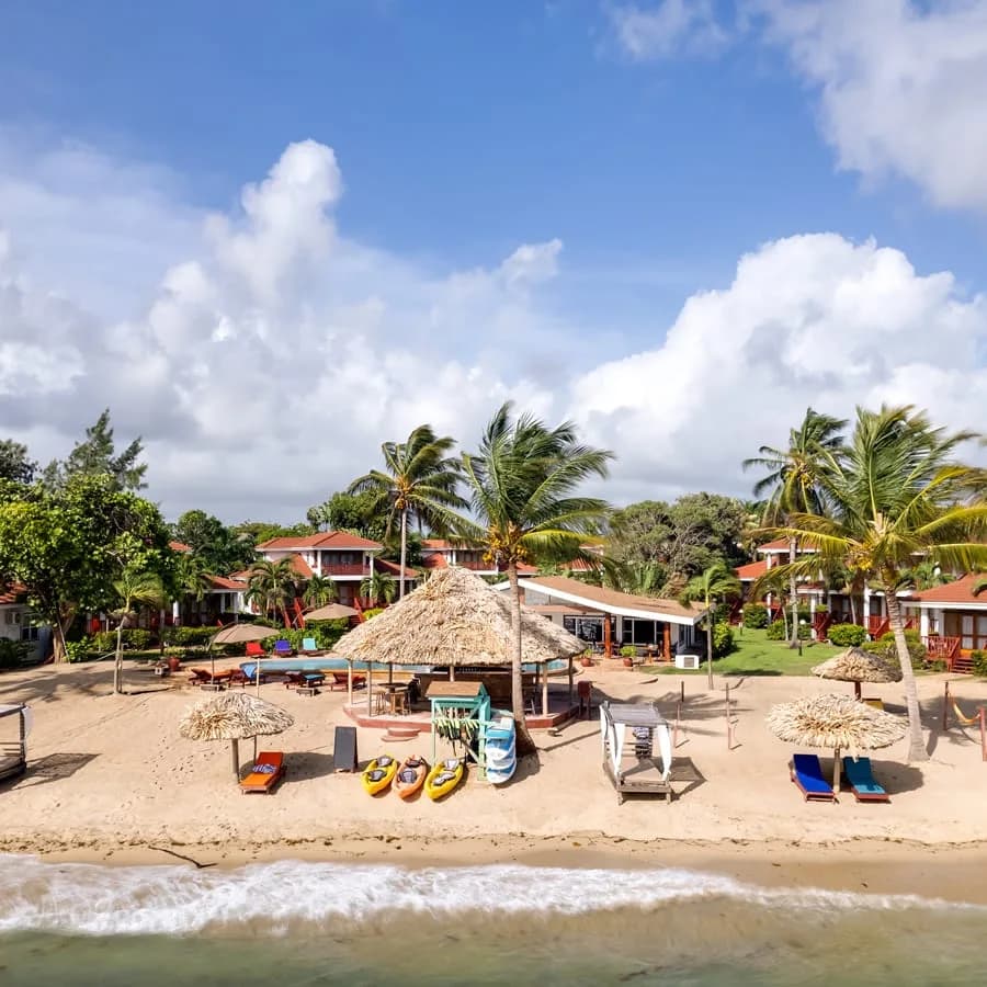 Belizean Dreams Resort beachfront in Hopkins, Belize with thatched-roof bar, kayaks, and colorful villa balconies