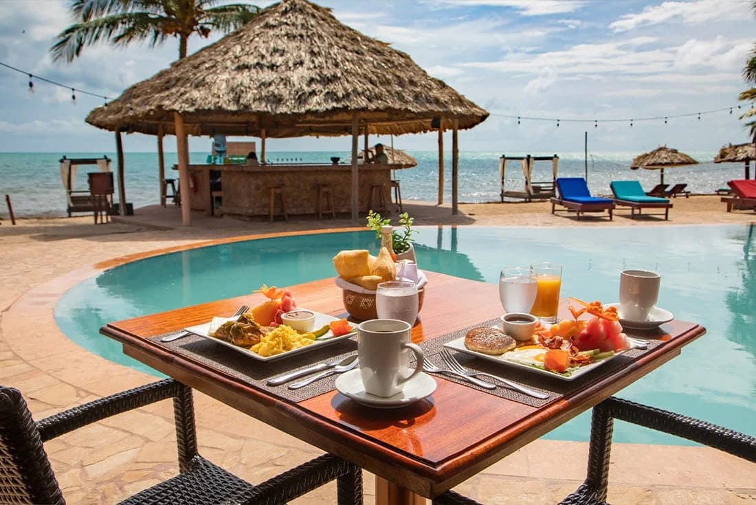 Beachfront thatched-roof tiki bar and loungers overlooking the ocean at Belizean Dreams Resort