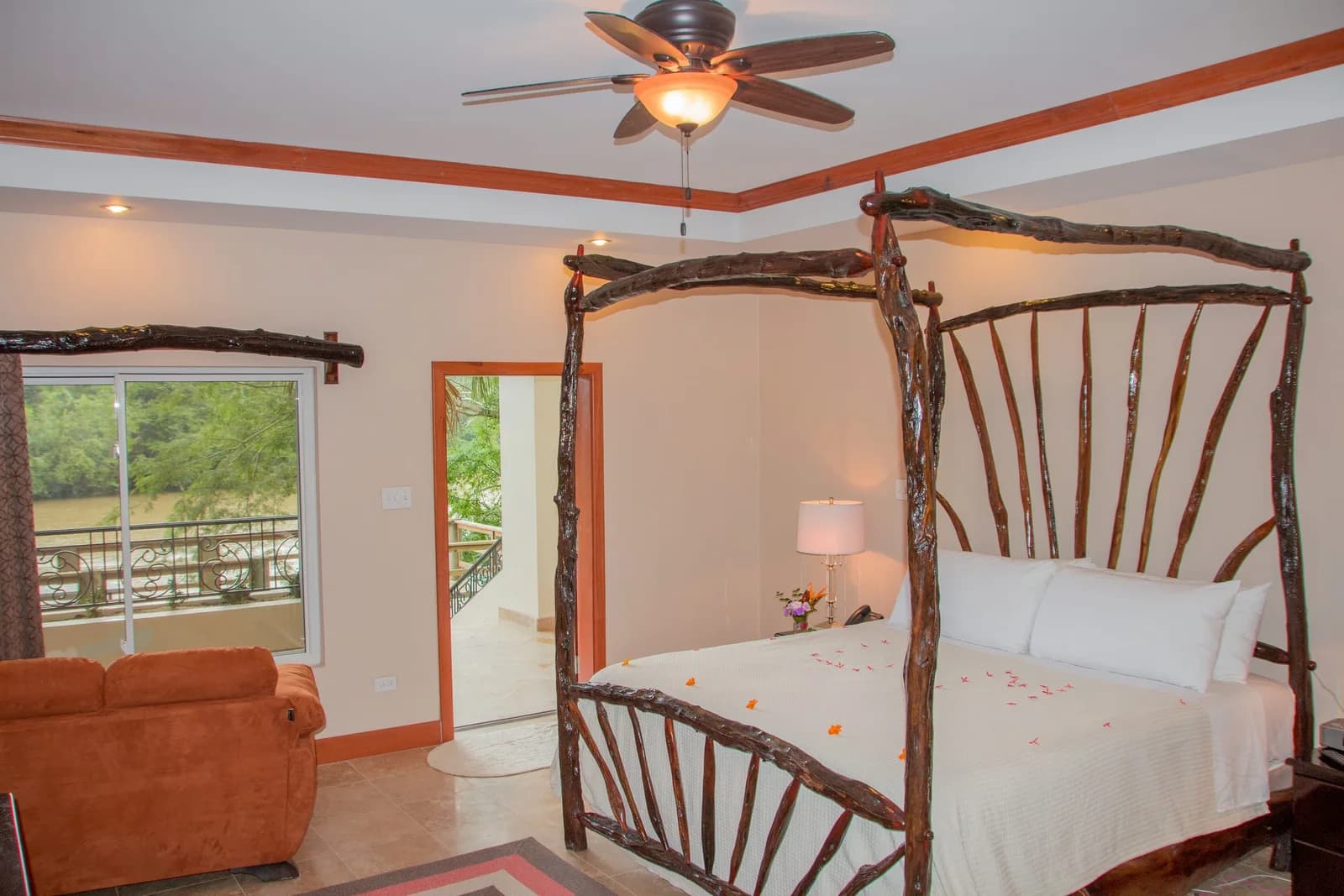 Guest room at Black Orchid Resort with a wooden canopy bed, sofa, and large windows overlooking greenery.