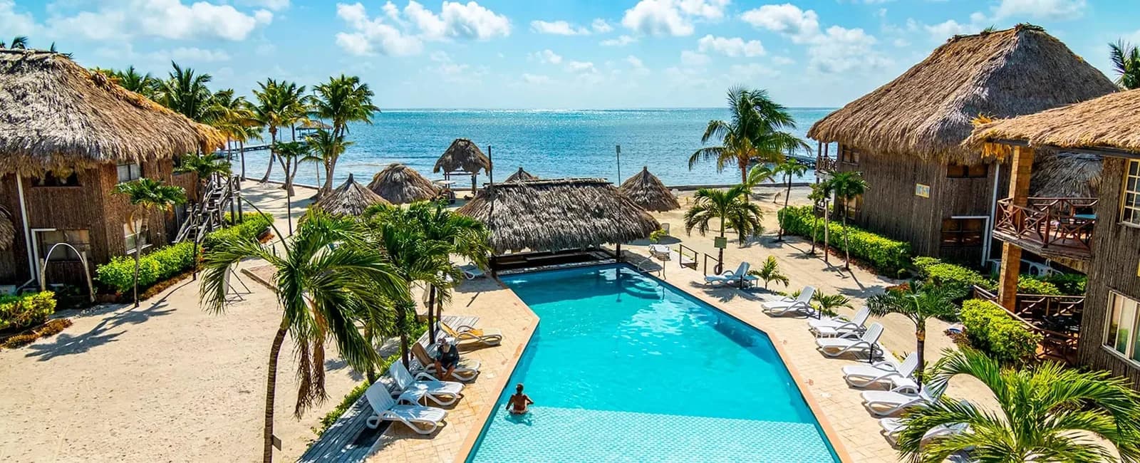 Swimming pool at Captain Morgan's Retreat framed by guest buildings and thatched palapas with the Caribbean Sea beyond