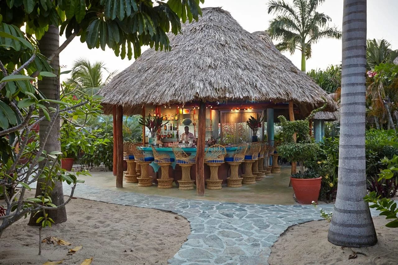 Thatched-roof bar at Chabil Mar Villas set among palm trees at dusk