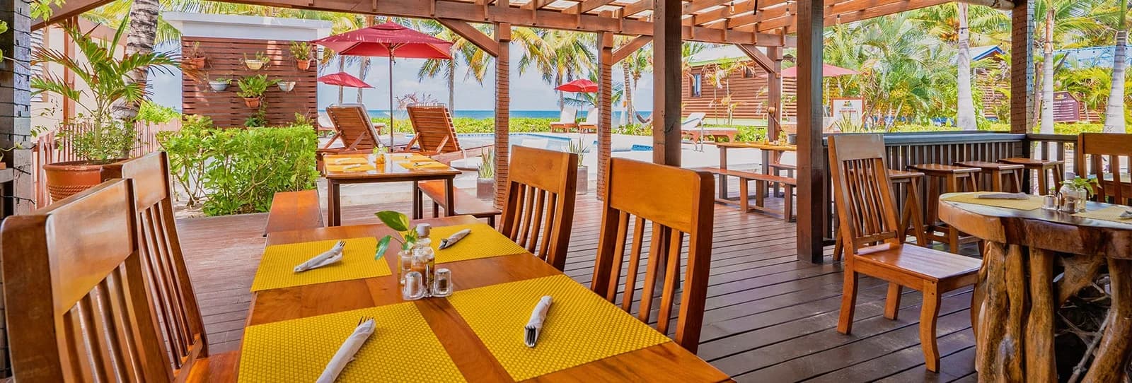 Covered dining deck at The Coconut Husk Restaurant at Coconut Row Boutique Hotel with yellow placemats and pool and ocean views
