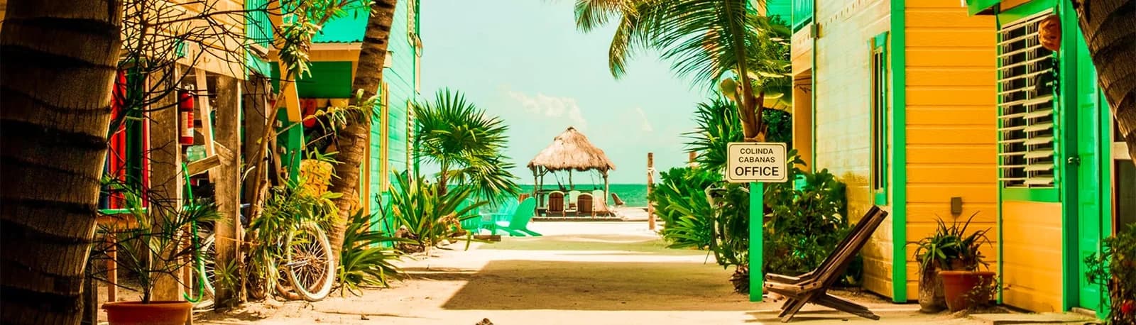 Sandy walkway between colorful cabanas leading past the Colinda Cabanas office sign to the beach palapa