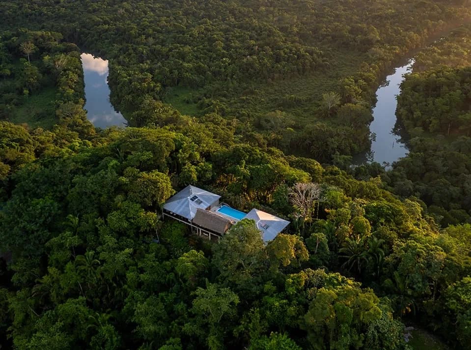 Drone view of Copal Tree Lodge's rooftops and pool surrounded by rainforest with the Rio Grande River winding through the jungle, Punta Gorda, Belize