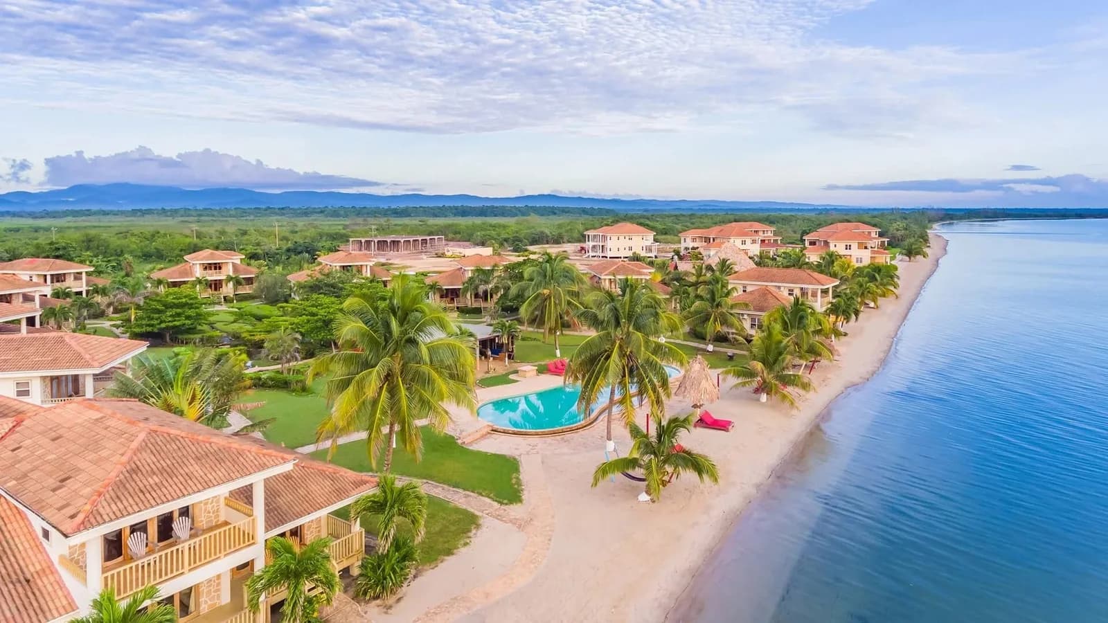 Wide aerial view of the full Hopkins Bay Belize property, showing rows of beach houses, a swimming pool, and the shoreline