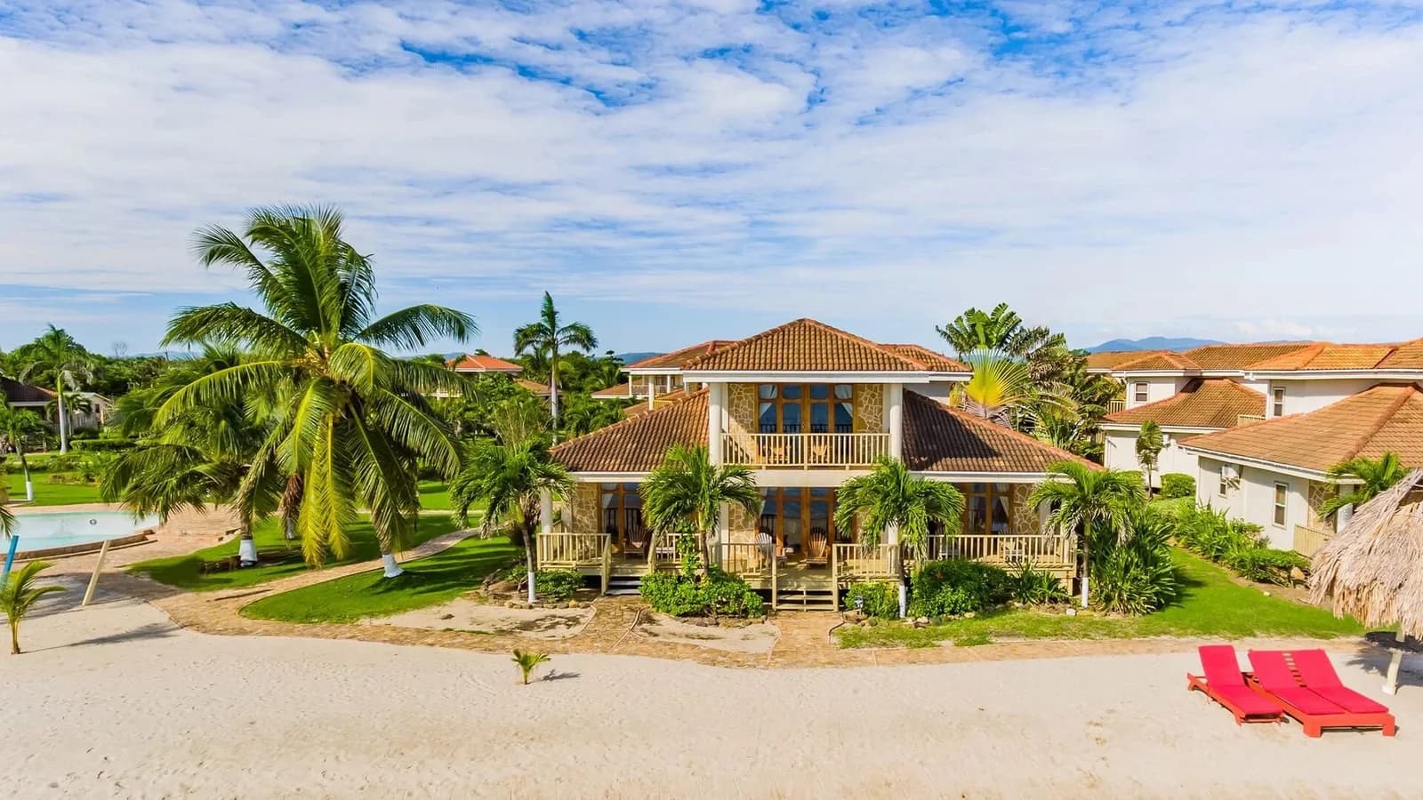 Aerial view of a two-story Hopkins Bay Belize beach house with red loungers on the sand out front