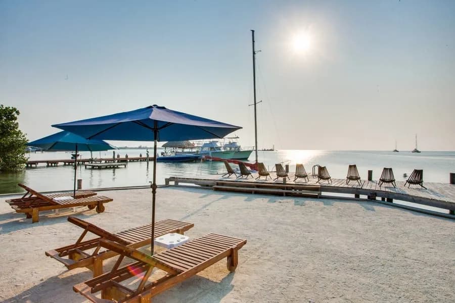 Private beach and dock with lounge chairs, umbrellas, and moored sailboats at Iguana Reef Inn, Caye Caulker, Belize