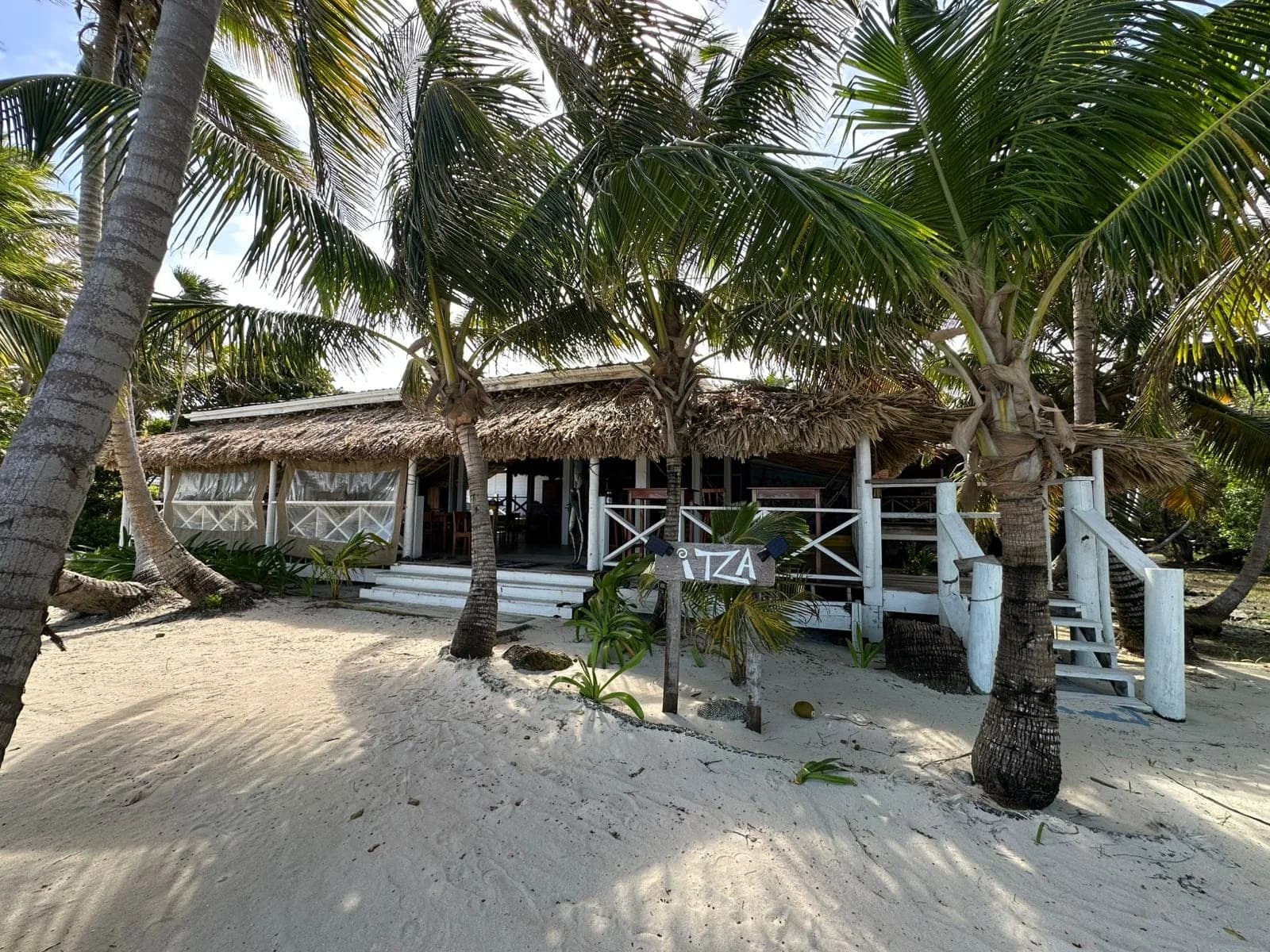 Thatched-roof open-air dining and lounge building at Itza Resort on Long Caye, Lighthouse Reef Atoll, Belize, with the ITZA sign on the beach