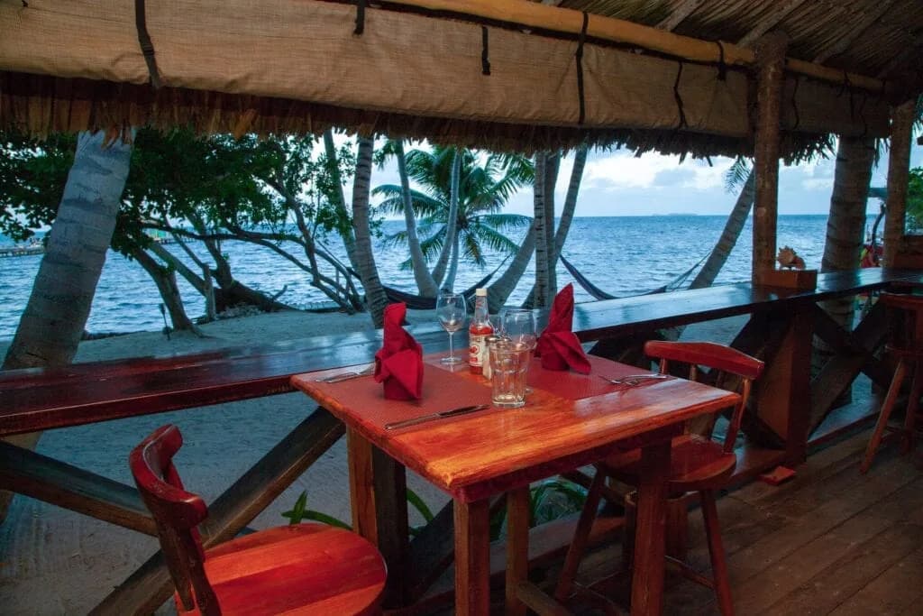 Beachfront dinner table set under a palapa roof at Itza Resort at dusk, overlooking the Caribbean Sea