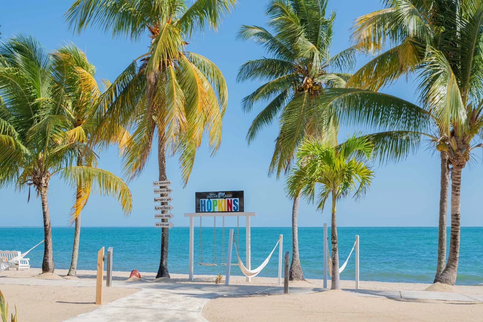 Palm-lined beachfront with hammocks and the Jaguar Reef Hopkins sign, Hopkins, Belize