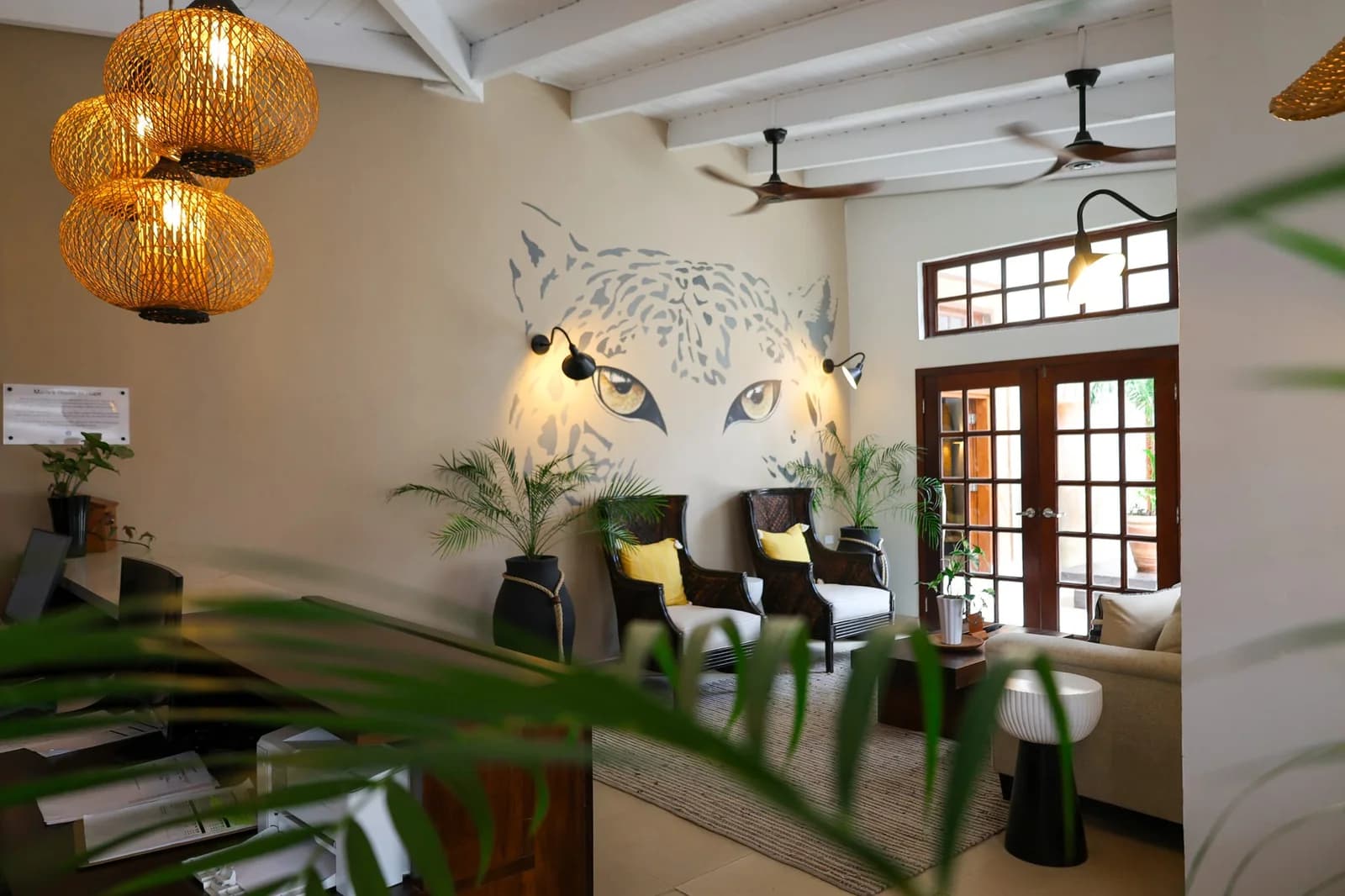 Lobby lounge with a jaguar mural, rattan pendant lights, and tropical plants at Jaguar Reef Lodge & Spa