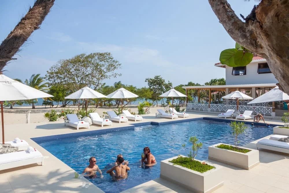 Guests relaxing in the oceanfront swimming pool with the beach and umbrellas behind, Naia Resort and Spa, Placencia, Belize