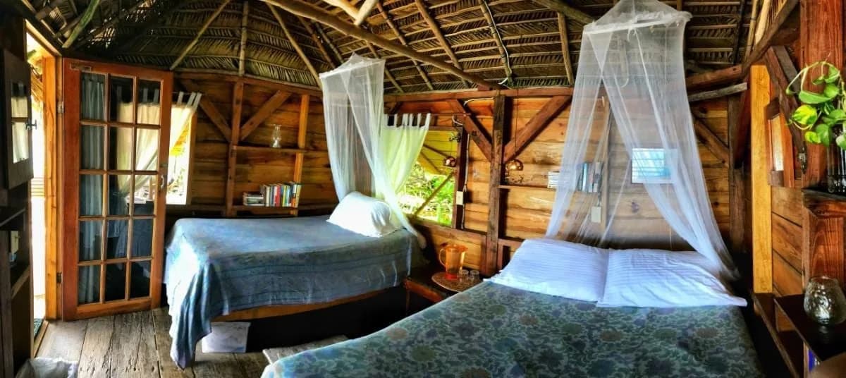 Rustic thatched-roof cabana bedroom with mosquito nets at Off The Wall Dive Center & Resort