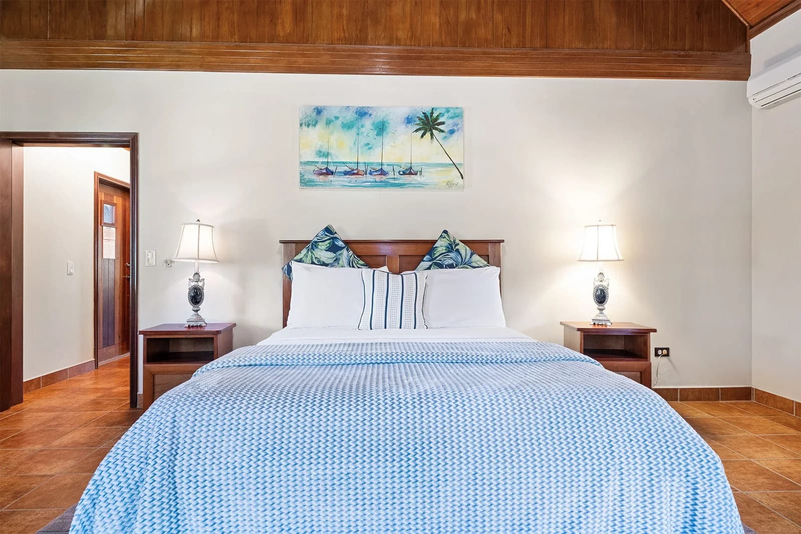 Bedroom in an Orchid Bay Resort condo with a queen bed, exposed wood-beam ceiling and tropical artwork