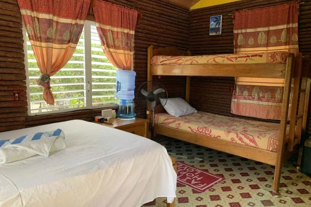 Inside a Palmento Grove cabin with a queen bed and a bunk bed, log walls and louvred windows