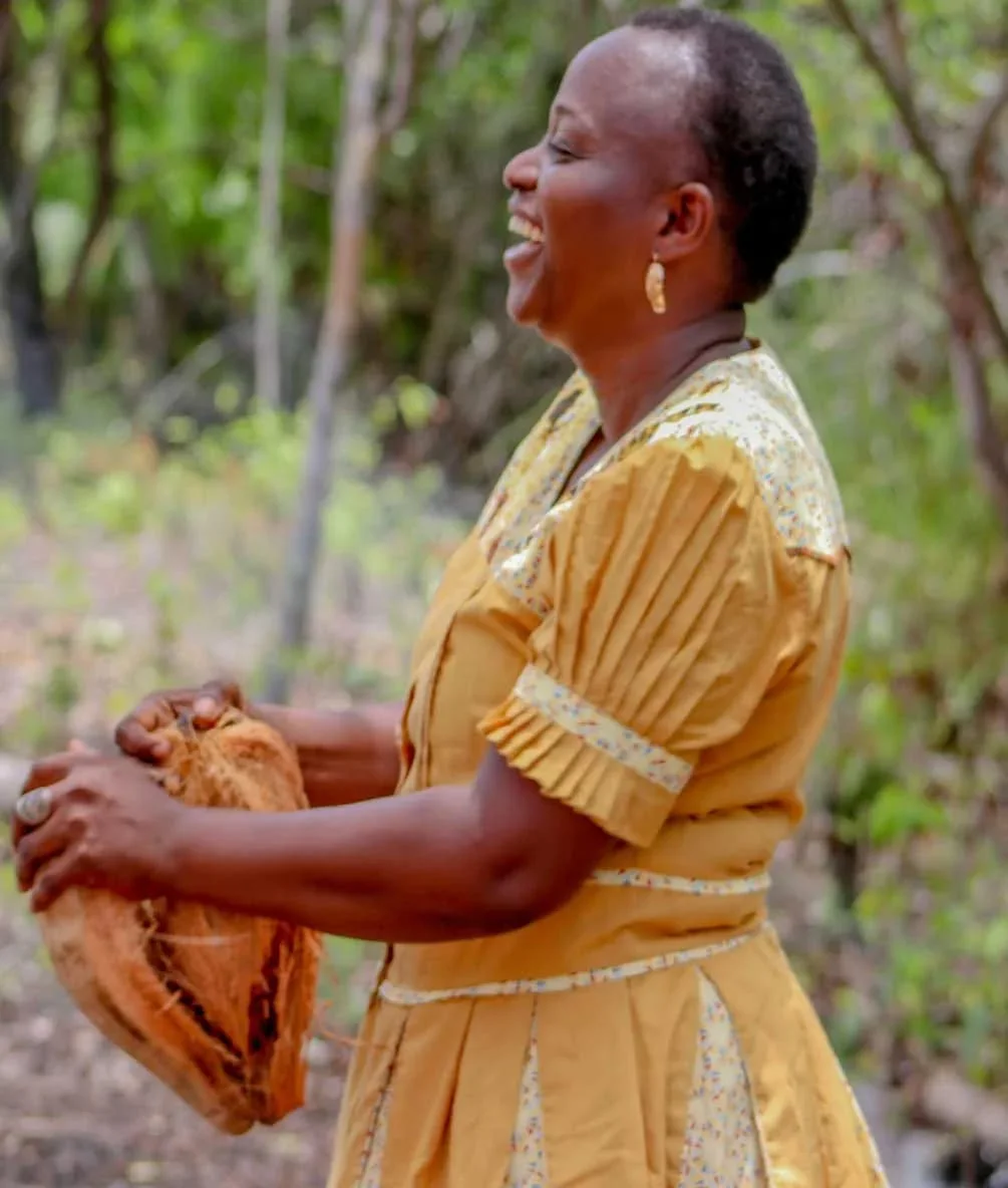 A Garifuna host at Palmento Grove husking a coconut in traditional yellow dress