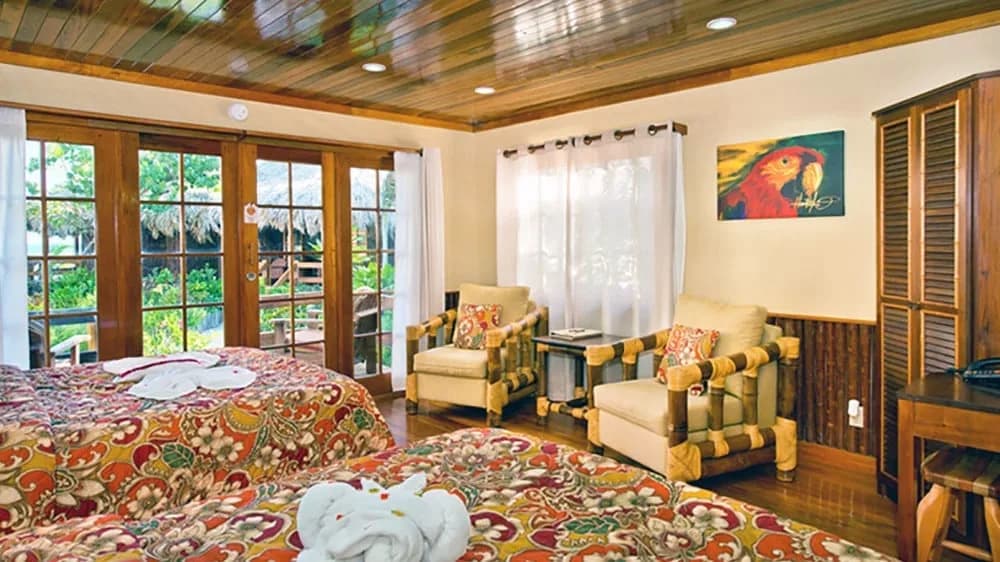 Ramon's Village Resort guest room interior with two floral-print beds, bamboo armchairs, and French doors opening onto a garden terrace, Ambergris Caye, Belize