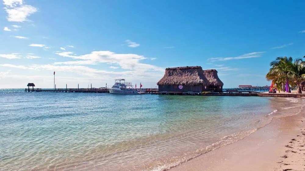 Calm turquoise beach in front of Ramon's Village Resort's overwater thatched dive shop hut and dock, San Pedro, Belize