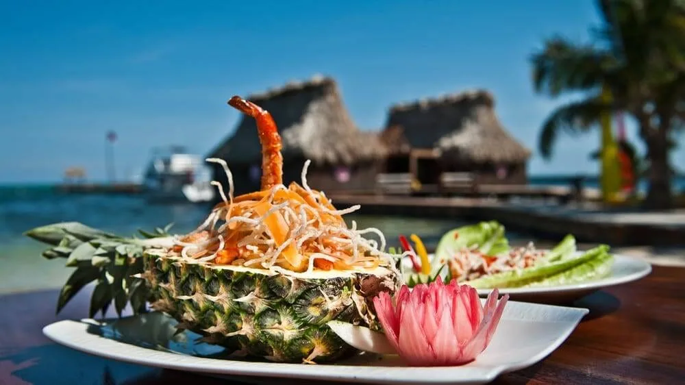 Pineapple-shrimp dish plated on the resort's restaurant table with the overwater thatched dock visible in the background, Ramon's Village Resort, Belize