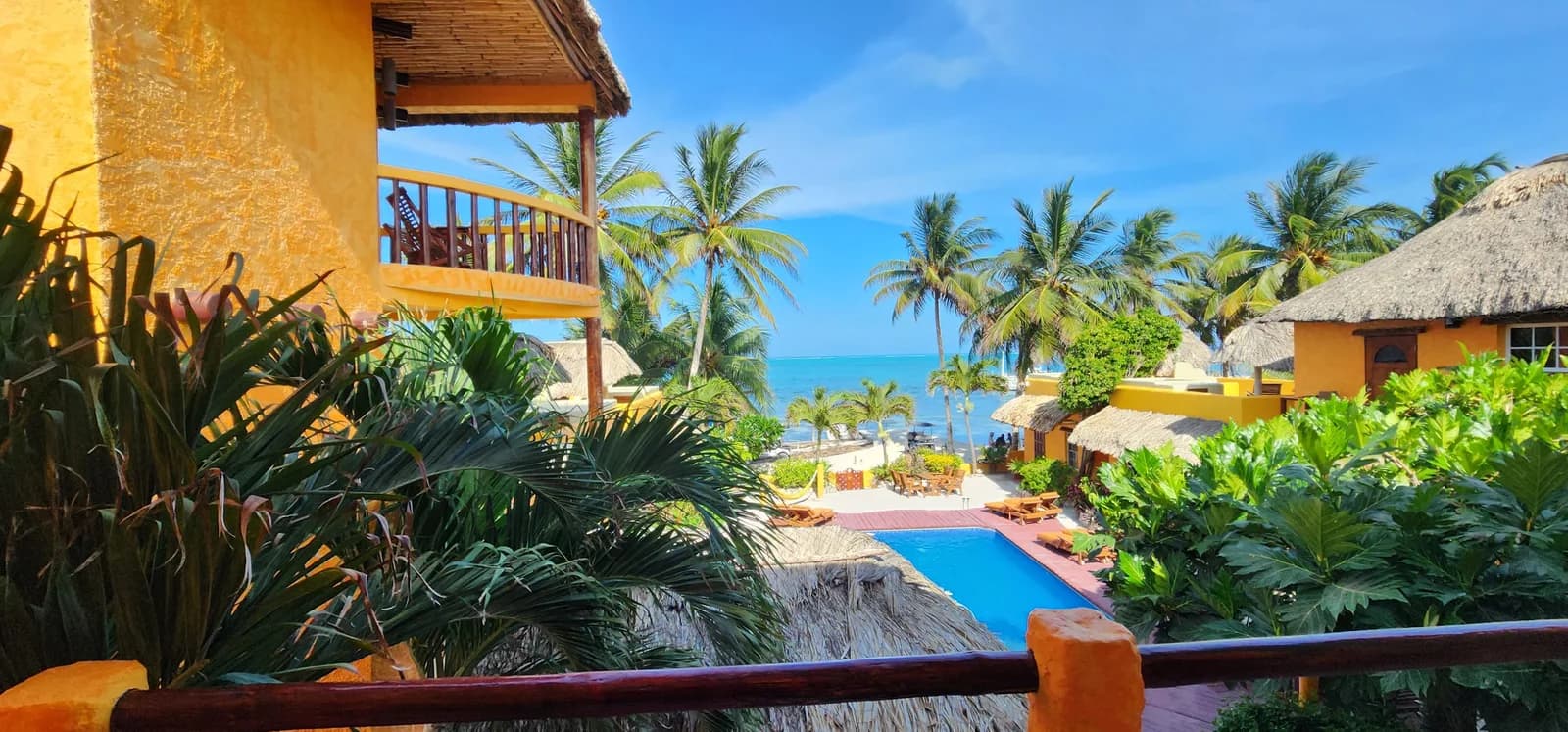 Elevated balcony view of the swimming pool, sun loungers and thatched beachfront palapas at Seaside Cabanas, Caye Caulker