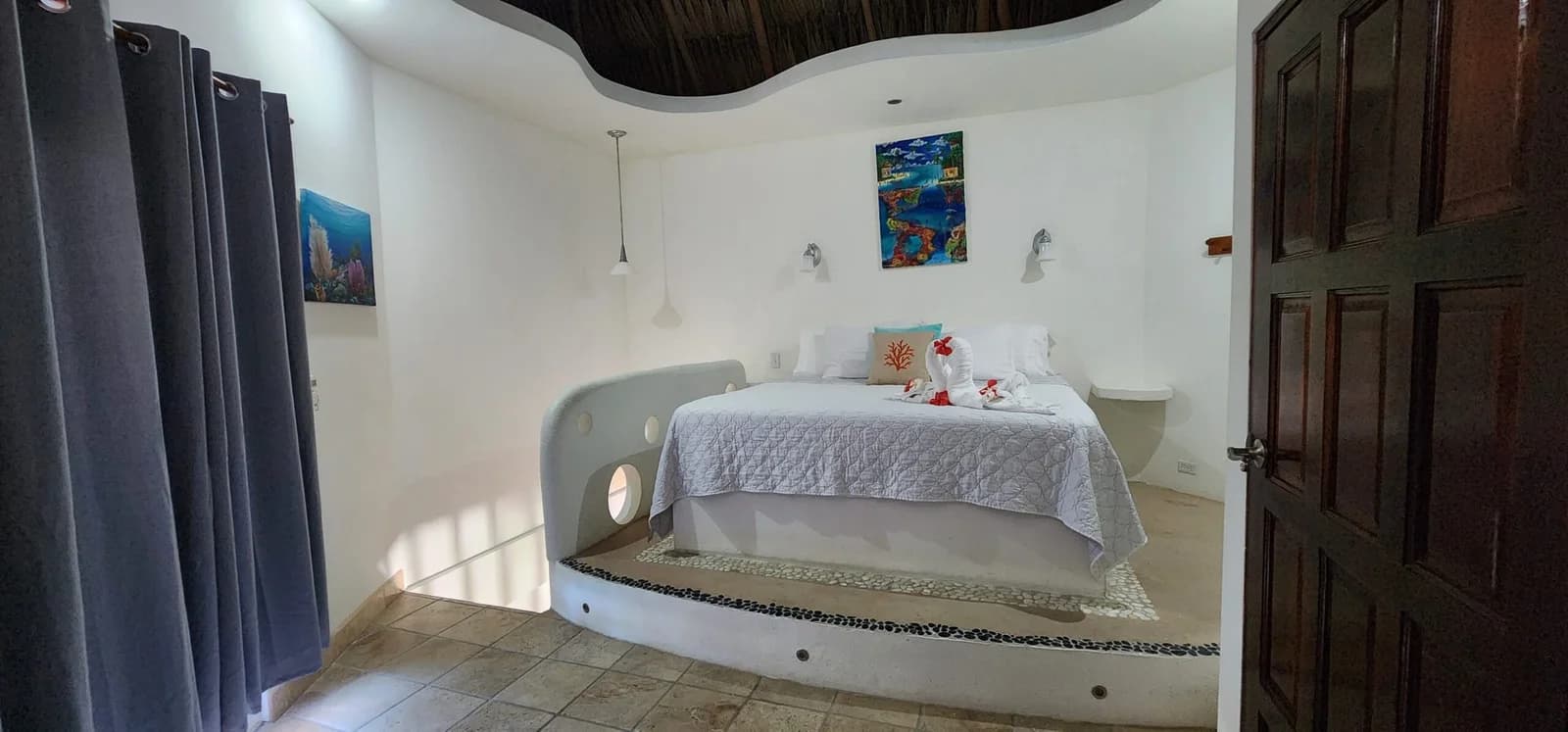 Curved, reef-inspired suite bedroom at Seaside Cabanas with a sculptural concrete bed platform and porthole cutouts