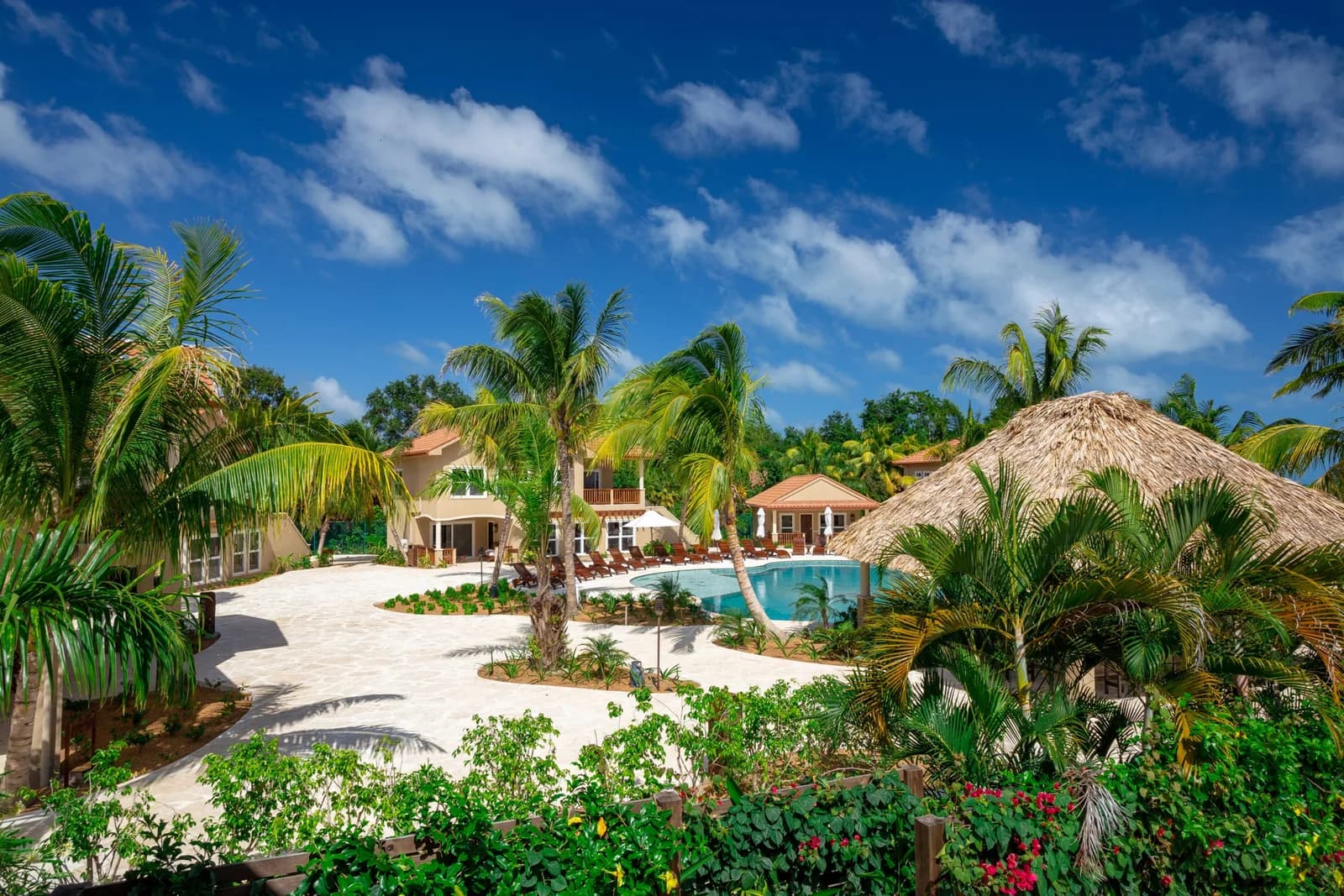 Resort pool and landscaped grounds surrounded by palm trees and a thatched palapa at Sirenian Bay Resort in Placencia, Belize