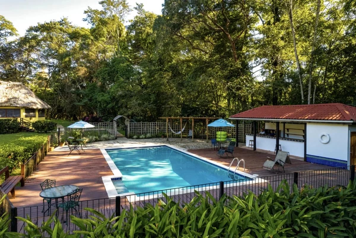Swimming pool deck at Tanager Rainforest Lodge with poolside bar and a yellow thatched cabana in the background