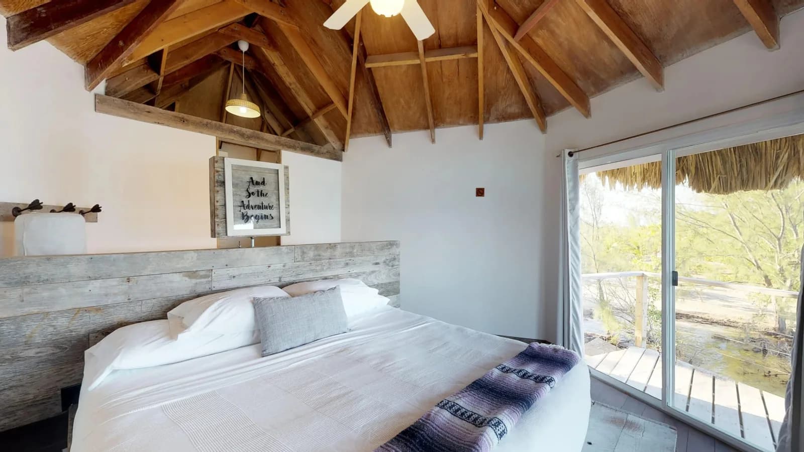 Bedroom interior of an overwater bungalow at Thatch Caye Resort with vaulted wood and palm thatch ceiling