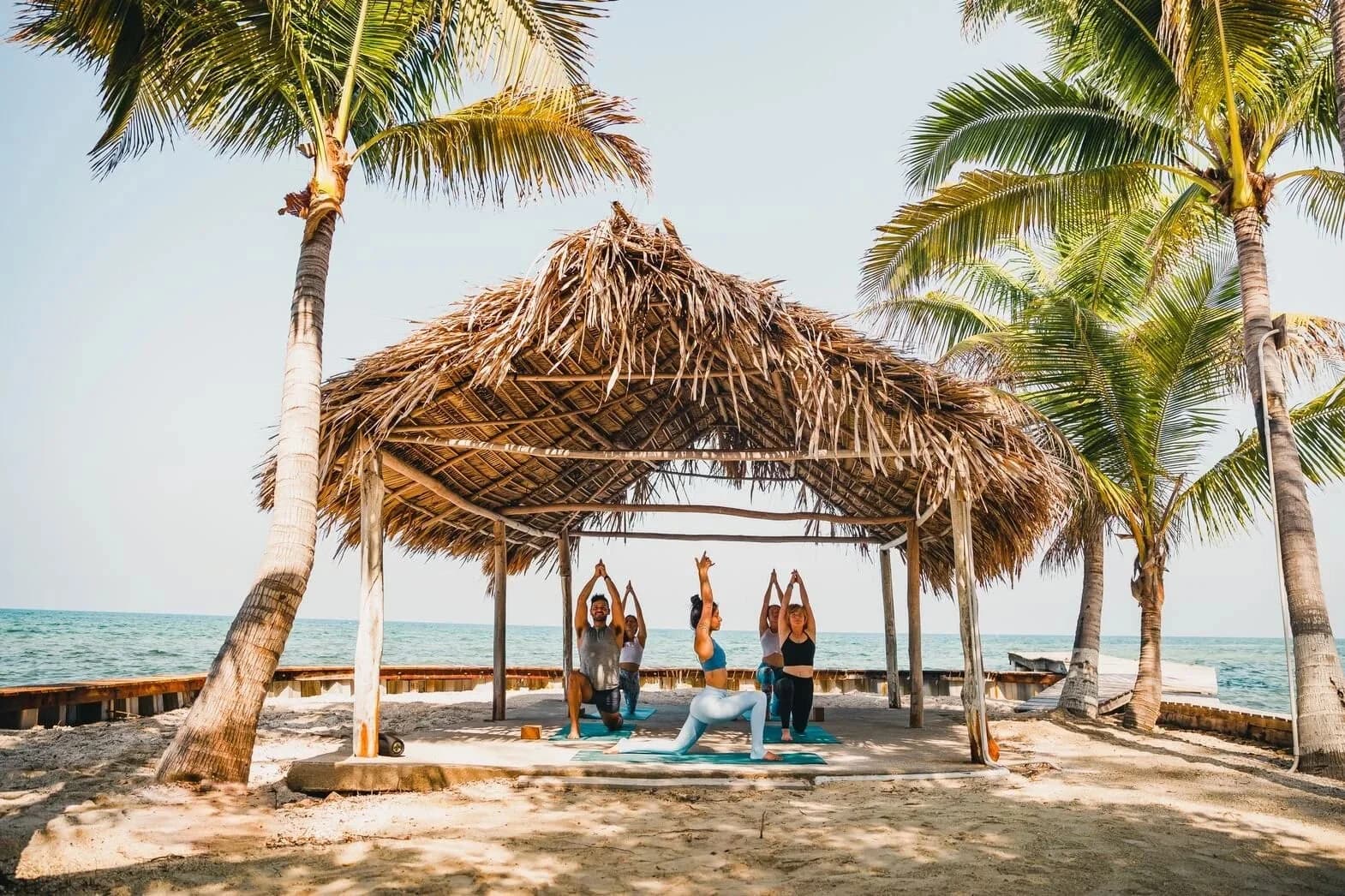 Guests practicing yoga under a palm-thatched palapa on the beach at Thatch Caye Resort