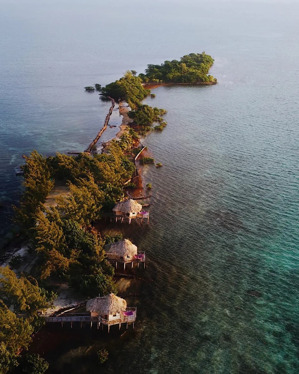 Aerial view of Thatch Caye's overwater bungalows lining the mangrove shoreline at sunrise