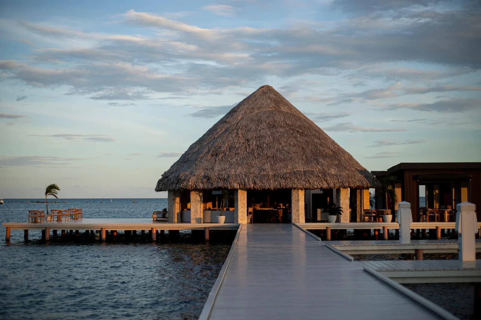 Thatched-roof, over-water Pier Lounge restaurant at The Placencia Resort at dusk, Belize