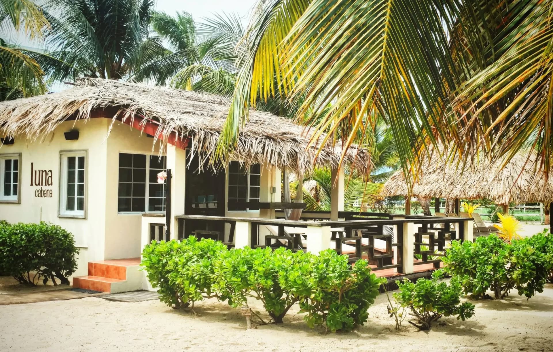 Luna Cabana at Caribbean Beach Cabanas, a whitewashed beachfront cabana with a thatched palapa roof and wooden deck in Placencia, Belize