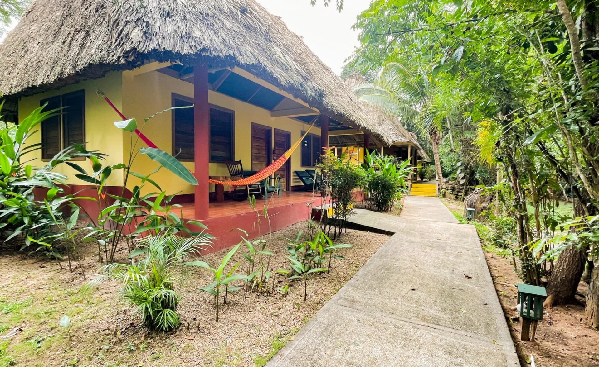 Thatched-roof cabana with a hammock strung across the porch and a garden path through the jungle grounds of Crystal Paradise Resort, Cristo Rey, San Ignacio, Belize