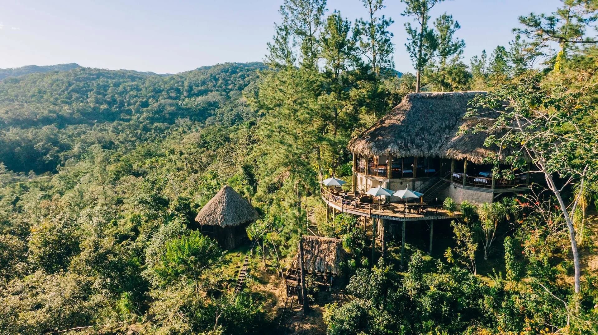 Aerial view of Gaia Riverlodge's thatched main lodge and a guest cabana perched in the Mountain Pine Ridge rainforest, Belize