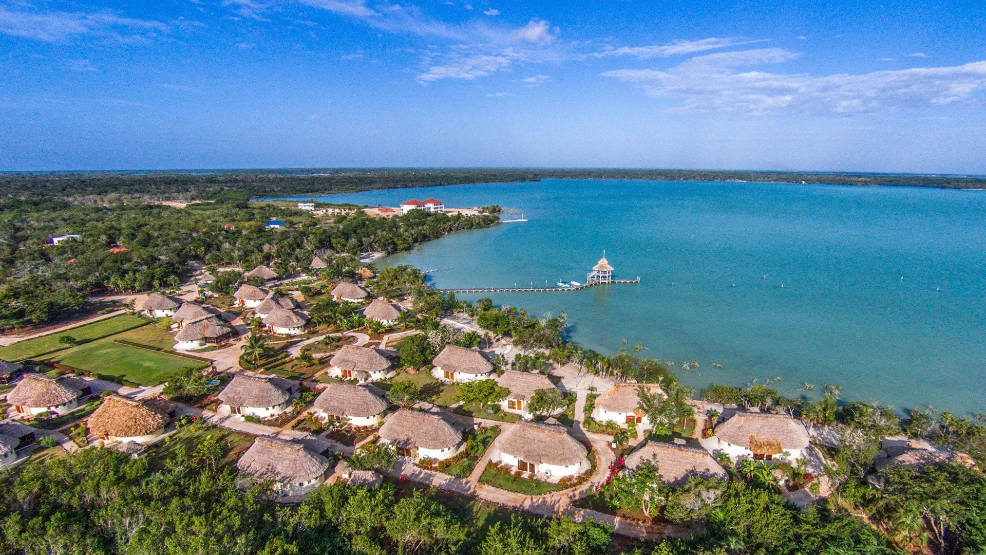 Aerial view of Orchid Bay Resort's thatched-roof casitas and condos lining the Chunox lagoon shoreline, with the resort's dock and gazebo extending into the water