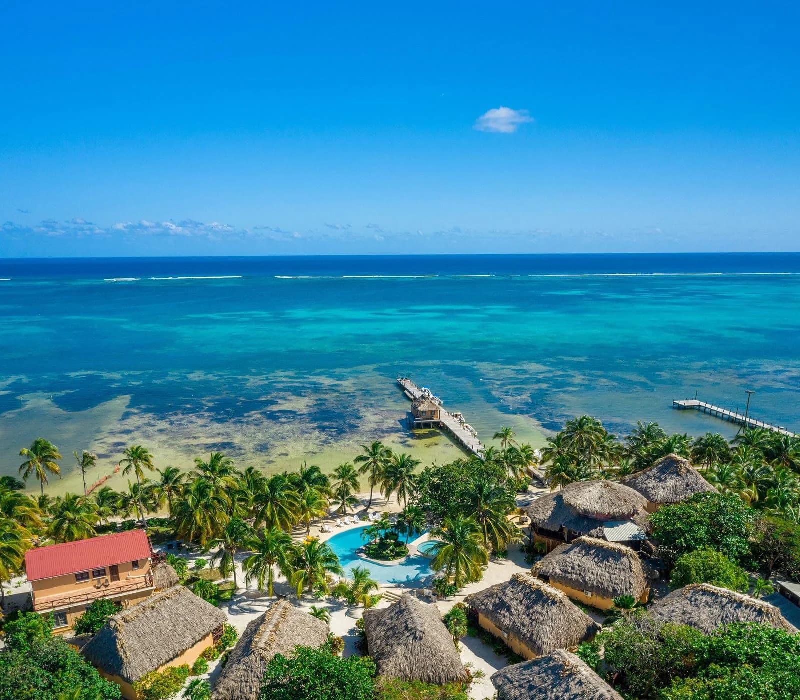 Aerial view of Portofino Beach Resort's thatched-roof cabanas, pool, and dock on Ambergris Caye, Belize