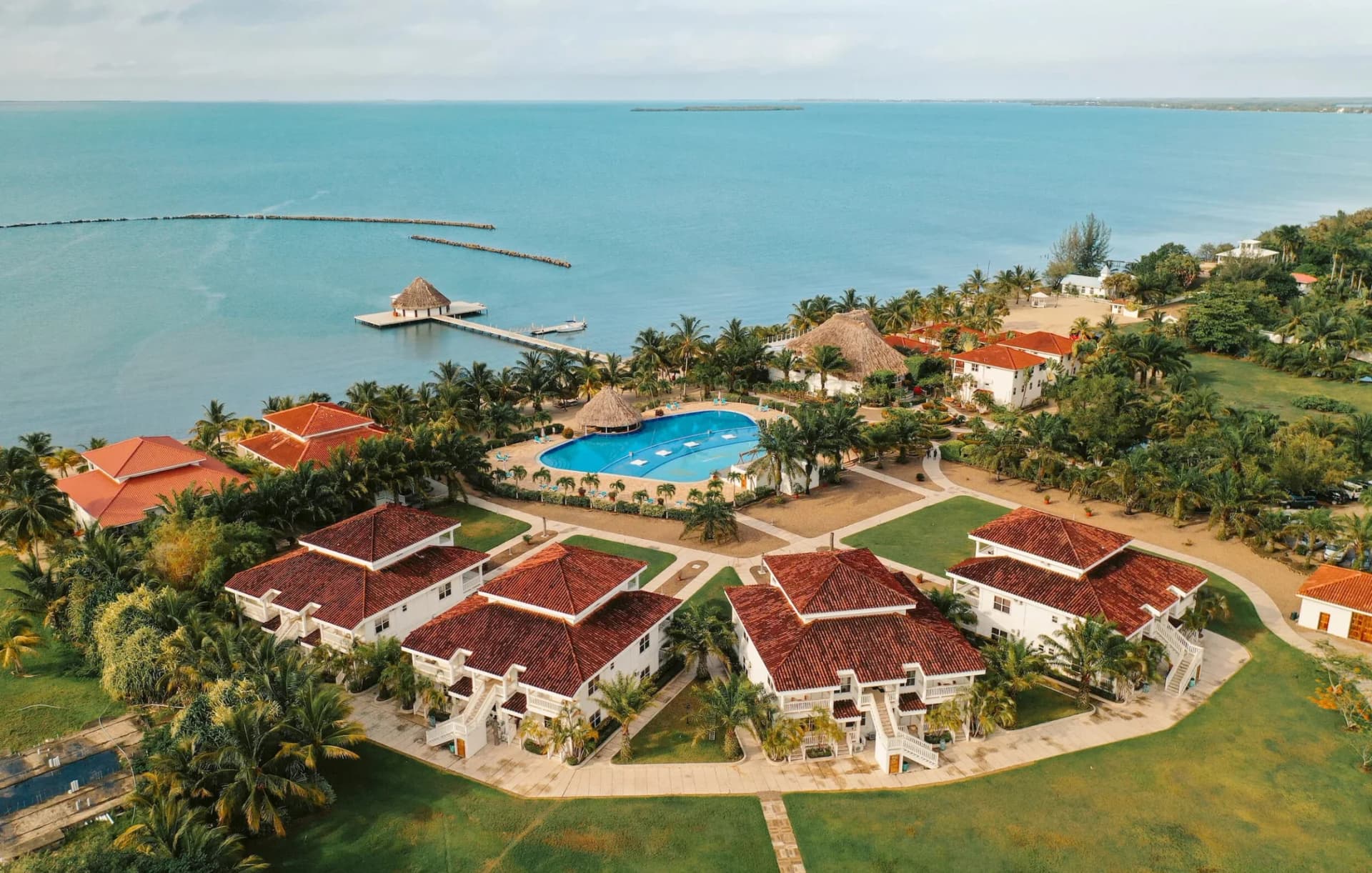Aerial view of The Placencia Resort showing its beachfront villas, swimming pool, and overwater pier restaurant on Maya Beach, Belize